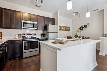A modern kitchen with a white island and dark brown cabinets.at Century Hampton Roads, Suffolk  